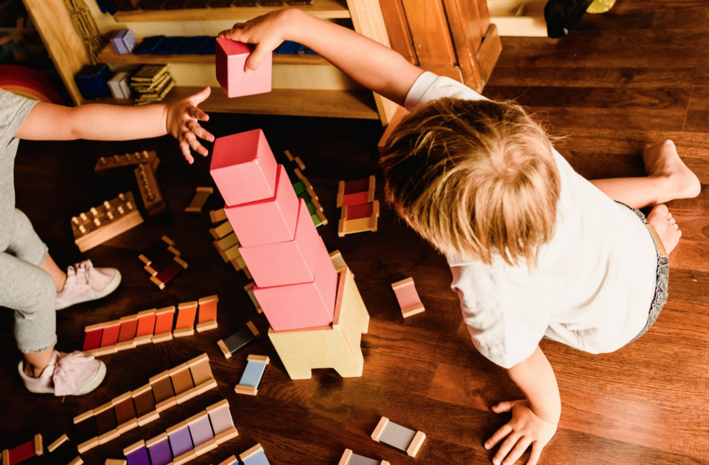 Two children build a tower with pink Montessori blocks.