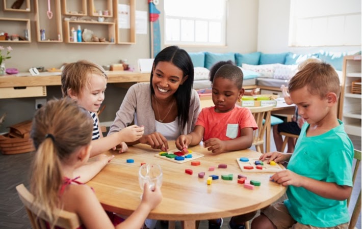 Teacher with four children sitting at a table using wooden shapes in a Montessori school