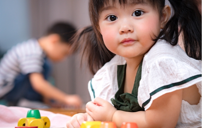 Young little girl laying down on the floor and playing colorful wooden Montessori sensorial toys