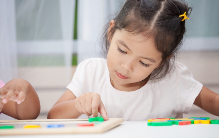 Young brunette girl focusing as she places a coloured magnet onto an associated play sheet.