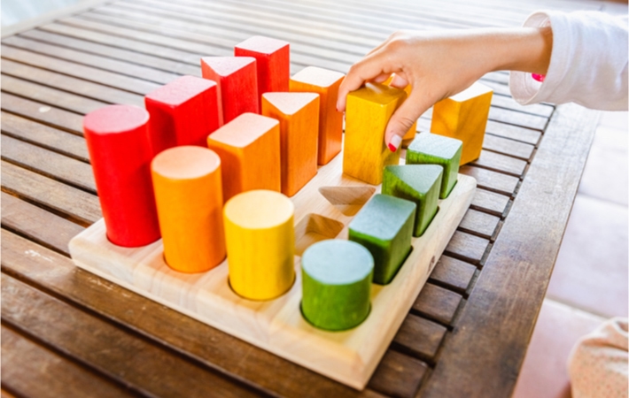 A child places blocks of arranges blocks of different shapes and sizes to practice colour, shape, and size grouping.