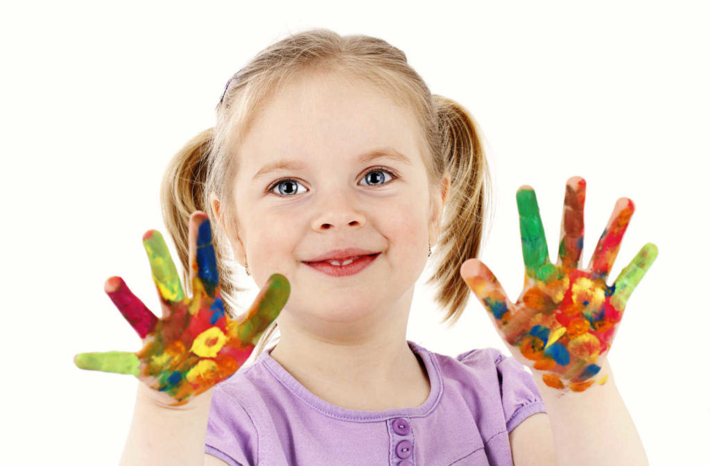 A female toddler in a Montessori is looking so happy with her hands full of colours.