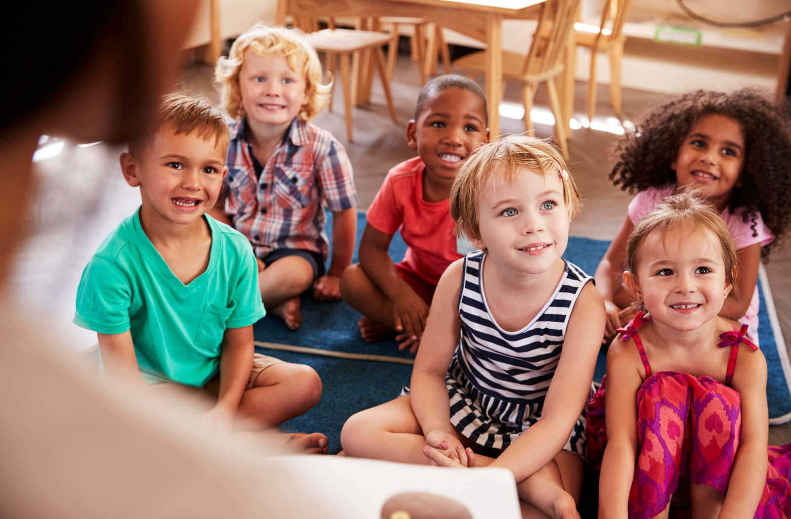 A group of kids sit on the floor and attentively listen to their teacher in a Montessori school.