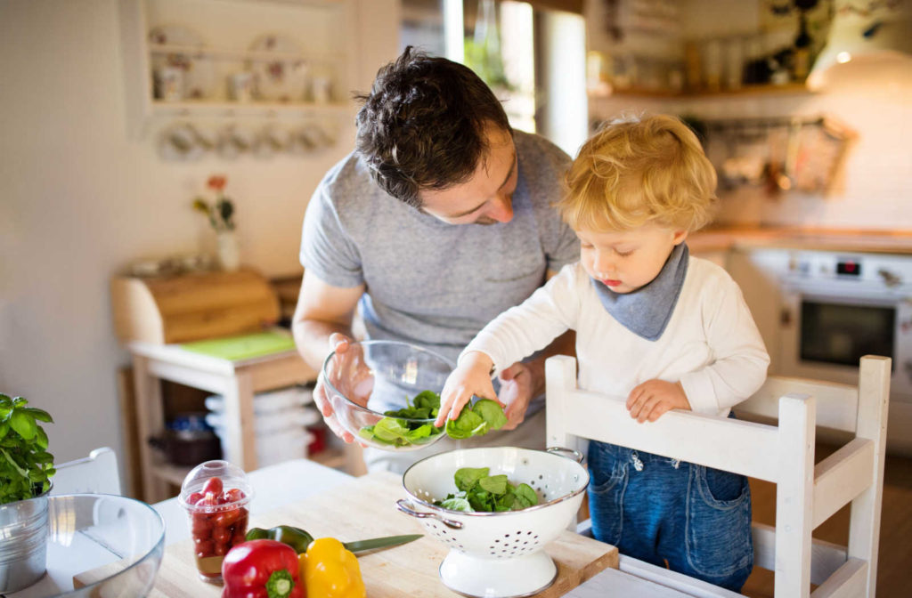 A young father and his toddler son cooking together in the kitchen, smiling and having a good time.