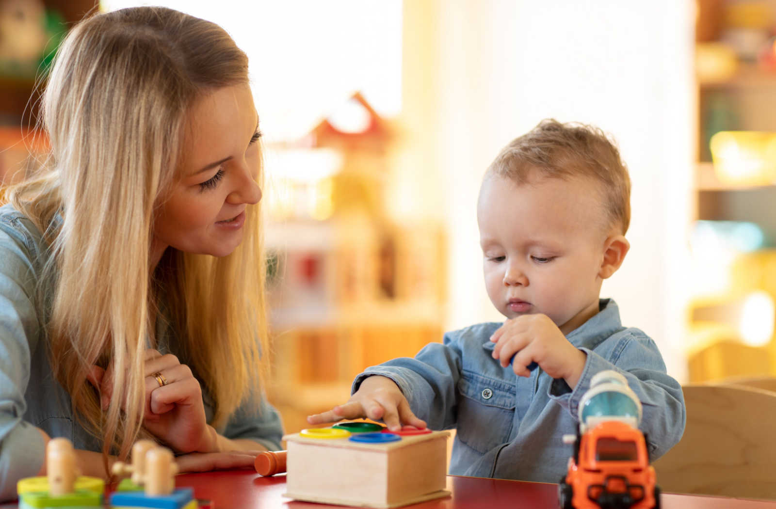 A baby playing with logical toys while an educator supervises and assists.