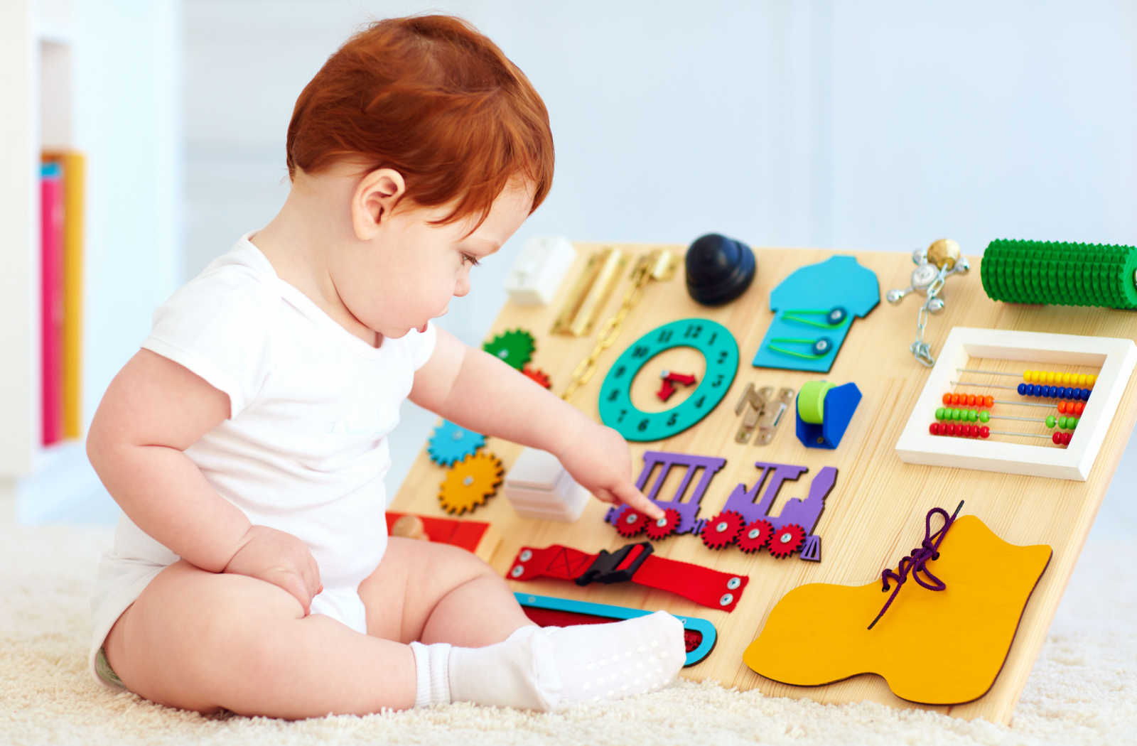A cute toddler baby playing with a busy board with various activities such as buttons, locks, and levers.