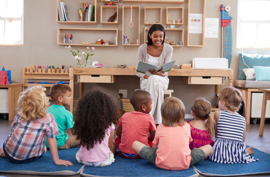 A female teacher at a Montessori school is reading a story to children.