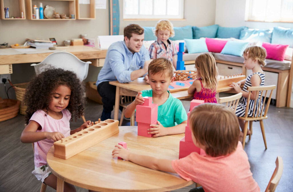 A teacher and his pupils working together at tables in a Montessori school classroom.