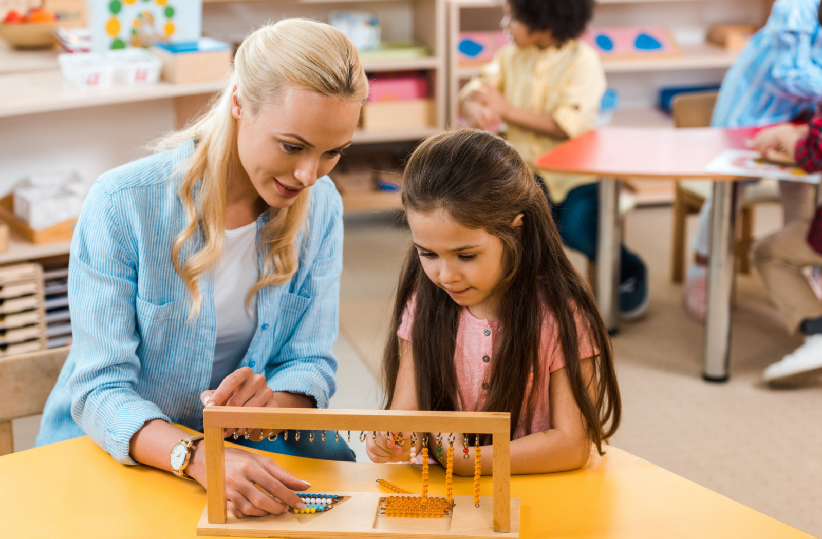 A female teacher doing a beading activity with a female child in a classroom.