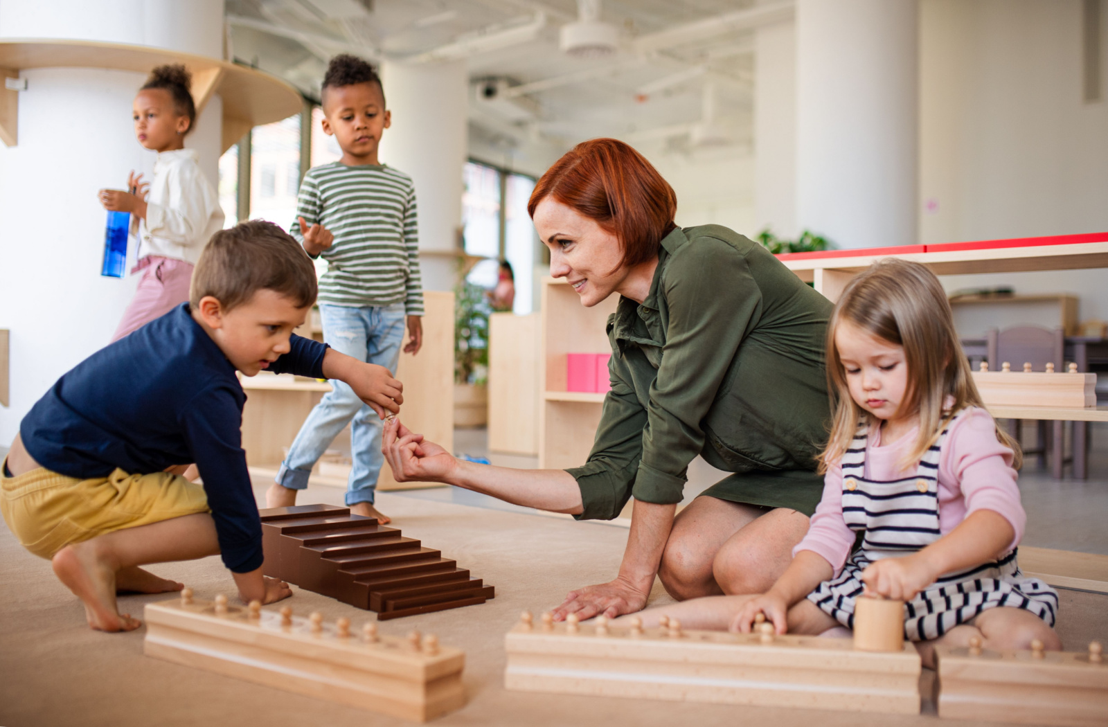 A teacher and her pupils working together and sitting on the floor in a Montessori school classroom.