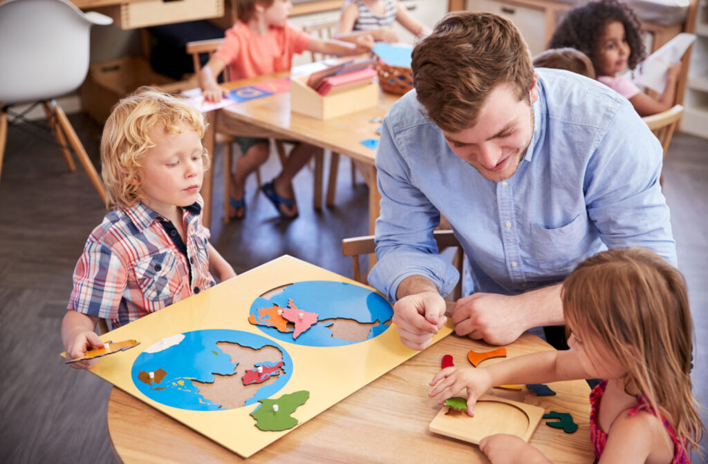 A teacher and his pupils working together at tables in a Montessori school classroom.