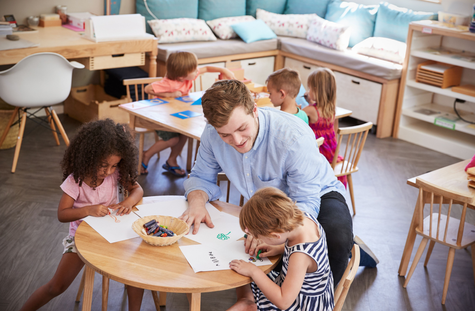 A teacher and her pupils working together and sitting on the floor in a Montessori school classroom.