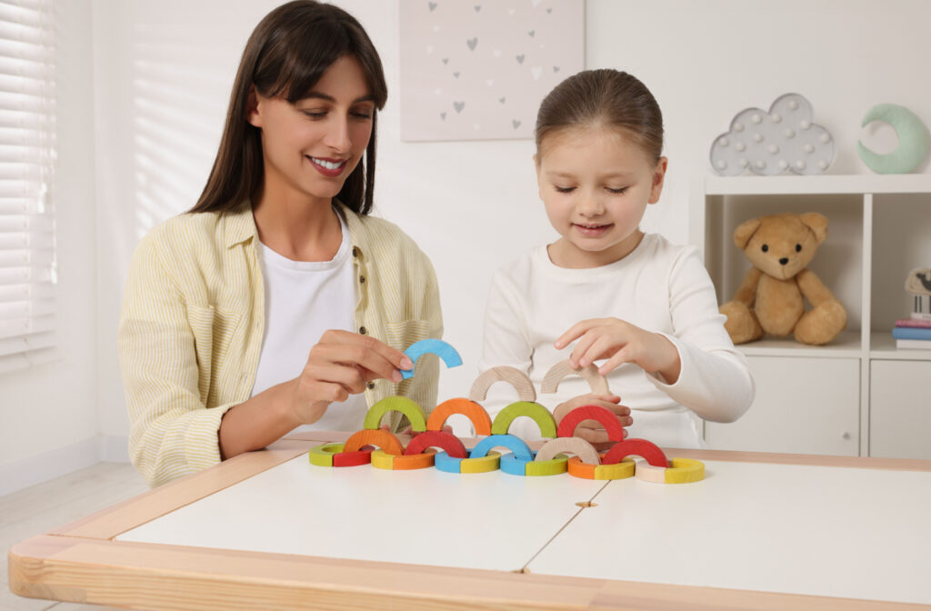A teacher helping a student develop motor skills by arranging wooden arc-shaped blocks on top of each other.