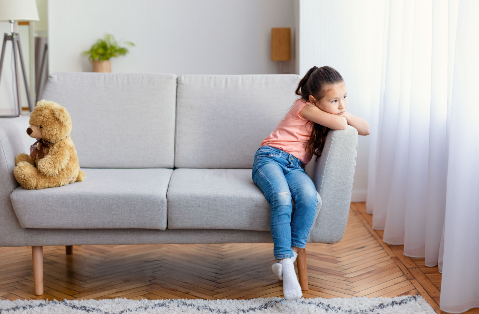 A young girl looking uninterested in playing with her teddy bear.