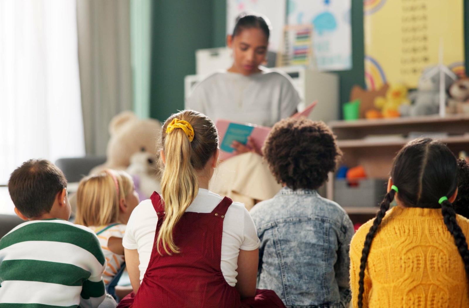 A Montessori teacher reading a book to a group of students sitting on the floor and listening intently.