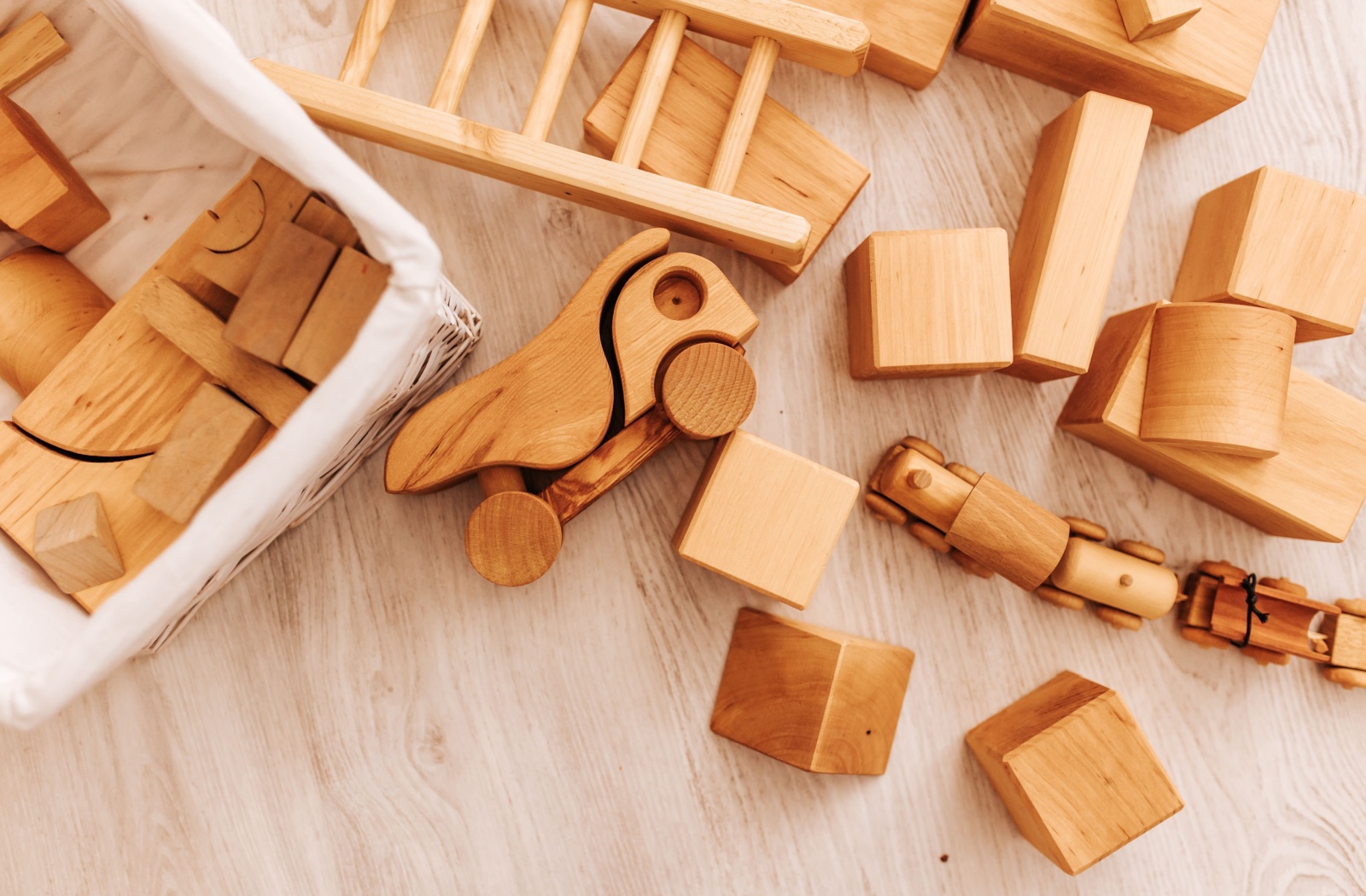Up close image of various wooden Montessori toys mixed up on the floor and in a white bin.