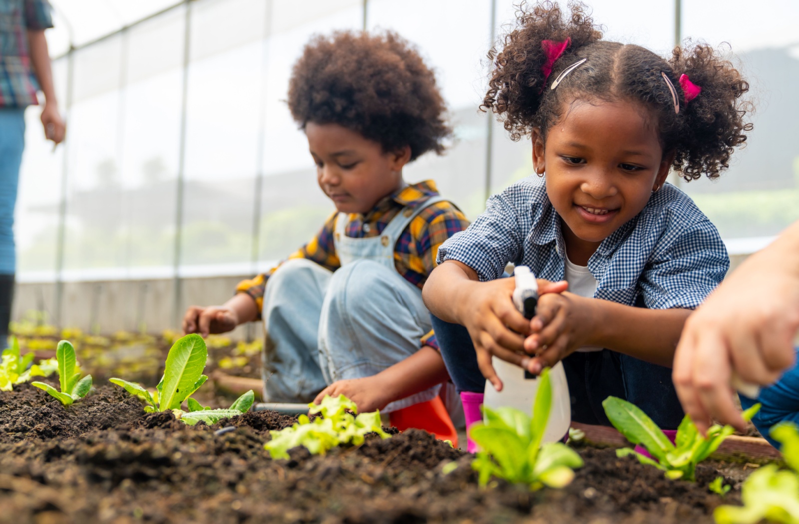 Two children care for plants in a garden, smiling and engaged.